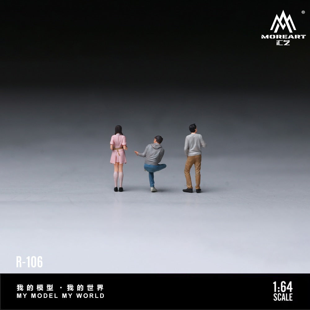 Three miniature 1:64 scale figure models from MOREART EZ, shown from behind on a dark-to-light gray gradient studio background. The figures represent three people wearing casual outfits: a pink dress, a gray hoodie and blue jeans, and a gray long-sleeve shirt and tan pants.