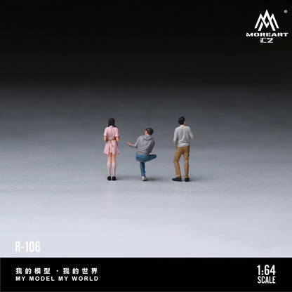 Three miniature 1:64 scale figure models from MOREART EZ, shown from behind on a dark-to-light gray gradient studio background. The figures represent three people wearing casual outfits: a pink dress, a gray hoodie and blue jeans, and a gray long-sleeve shirt and tan pants.